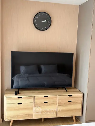 Modern bedroom with sleek TV setup and stylish wooden dresser under a wall clock.