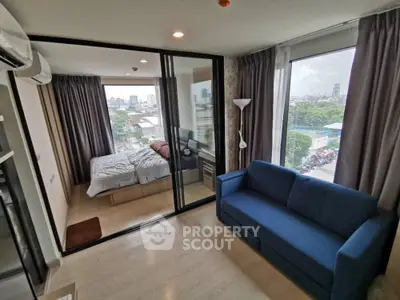 Modern apartment with glass-walled bedroom and city view, featuring a cozy blue sofa.