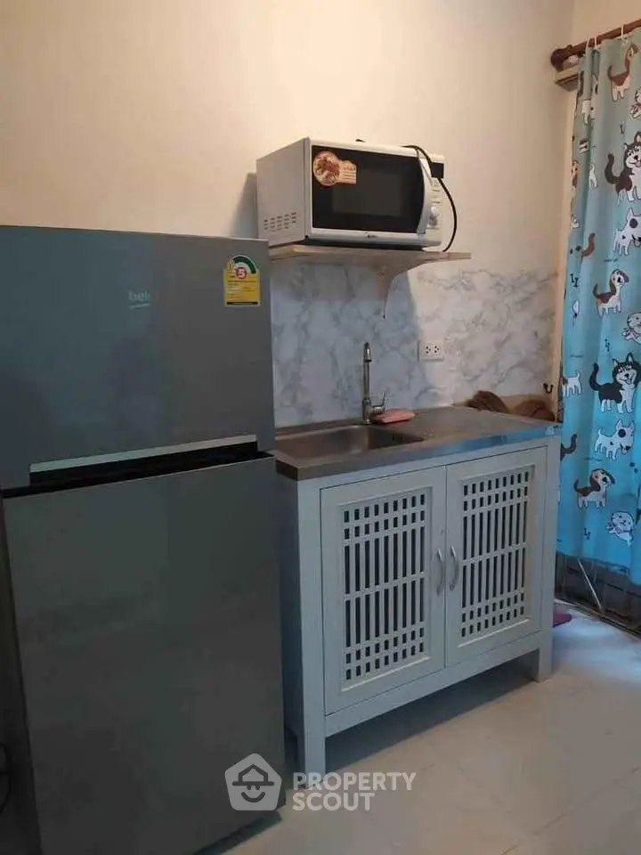 Compact kitchen with fridge, microwave, and stylish cabinetry in cozy apartment.