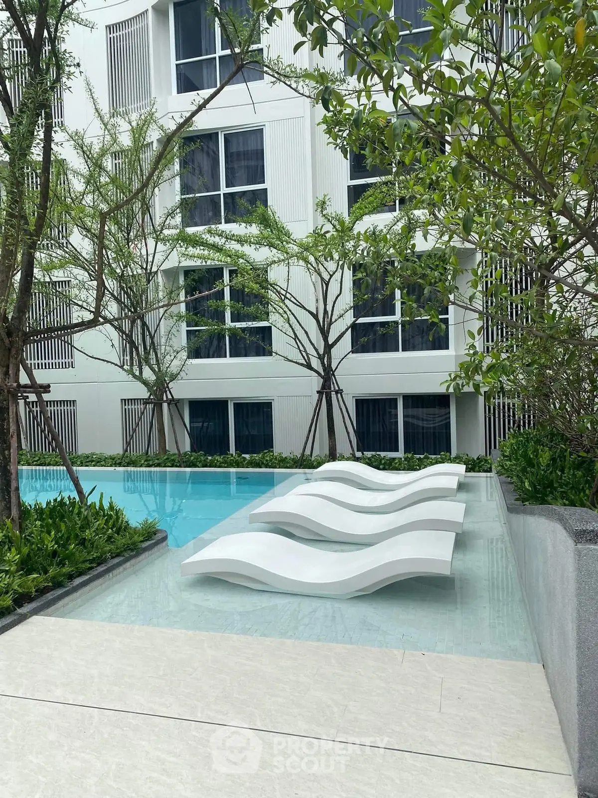 Luxurious poolside area with modern loungers and lush greenery in a contemporary building setting.