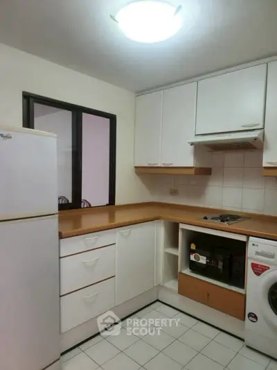 Modern kitchen with white cabinets, fridge, and washing machine in cozy apartment.