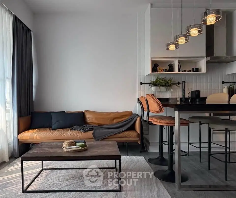 Modern living room with stylish leather sofa and open kitchen layout, featuring chic pendant lighting.