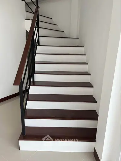 Modern staircase with sleek wooden steps and black railing in a contemporary home.