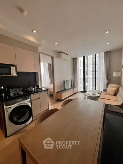 Modern open-plan living room with kitchen, featuring sleek appliances and large windows for natural light.