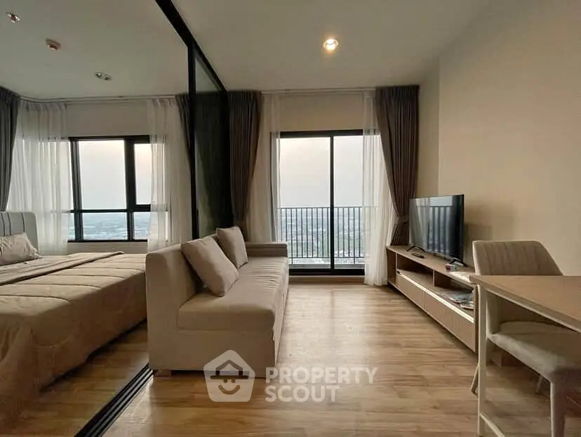 Modern living room with large windows and city view, featuring a cozy sofa and sleek TV setup.