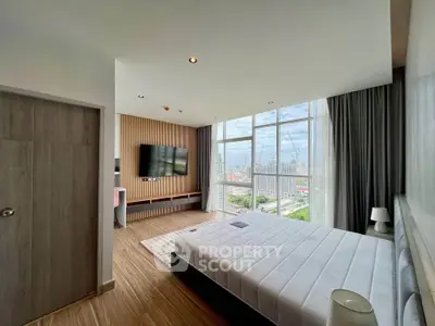 Spacious bedroom with floor-to-ceiling windows offering stunning city views, modern decor, and ample natural light.