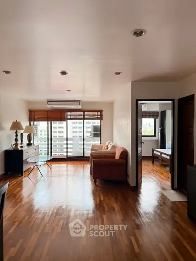 Spacious living room with wooden flooring and large windows offering city views