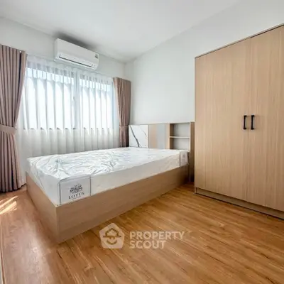 Modern bedroom with wooden flooring, large window, and sleek wardrobe in a bright apartment.