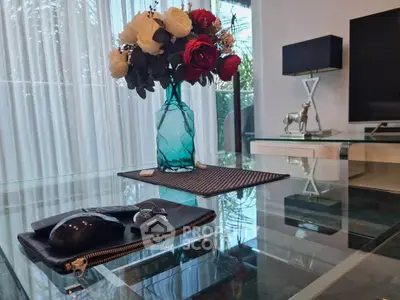 Elegant living room with glass table, floral centerpiece, and modern decor.