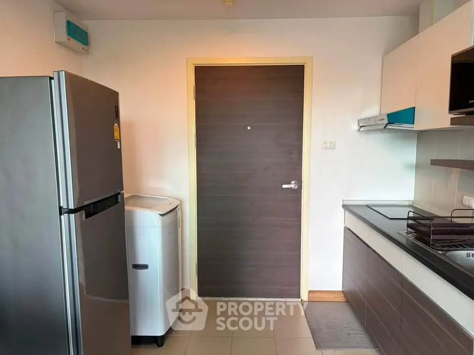 Modern kitchen with stainless steel fridge and washing machine, sleek cabinetry, and tiled flooring.