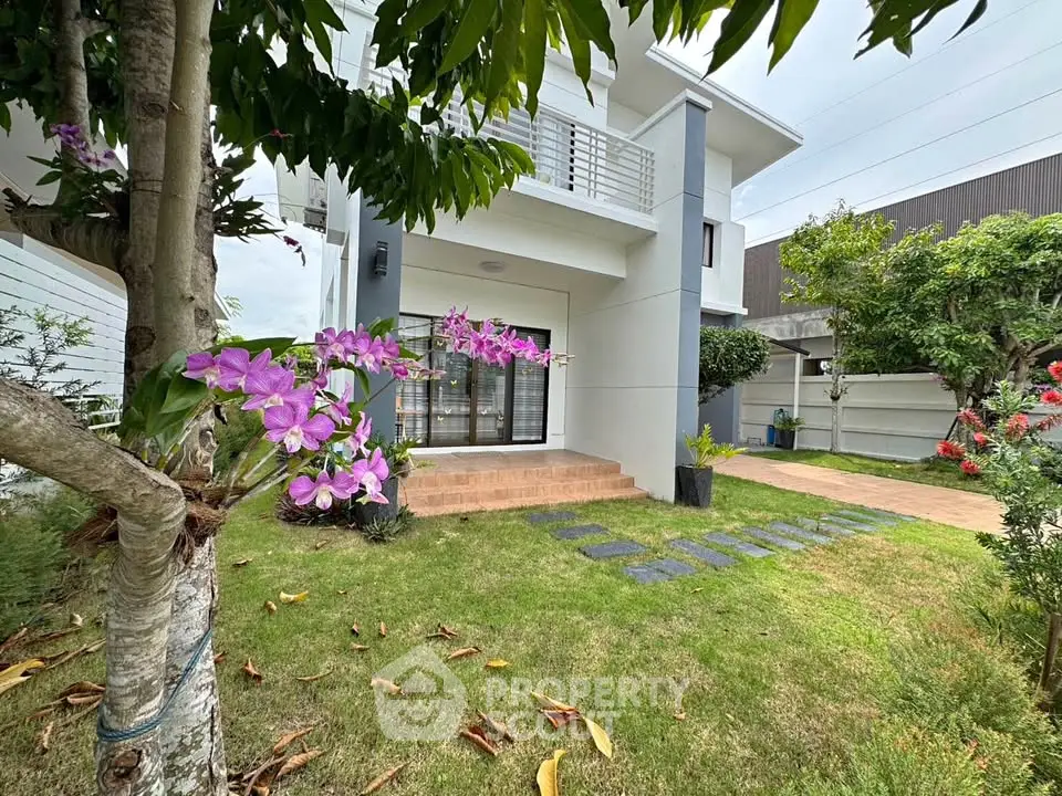 Modern two-story house with lush garden and elegant balcony, perfect for family living.