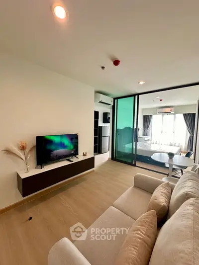 Modern living room with TV, cozy sofa, and large windows for natural light.