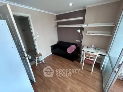 Cozy small living room with wooden flooring, black sofa, and wall-mounted shelves.
