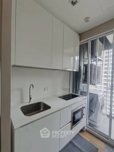 Modern compact kitchen with sleek white cabinets and built-in appliances, featuring a balcony view.