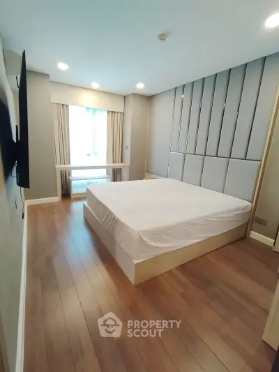 Modern bedroom with wooden flooring and stylish wall paneling, featuring a large window for natural light.