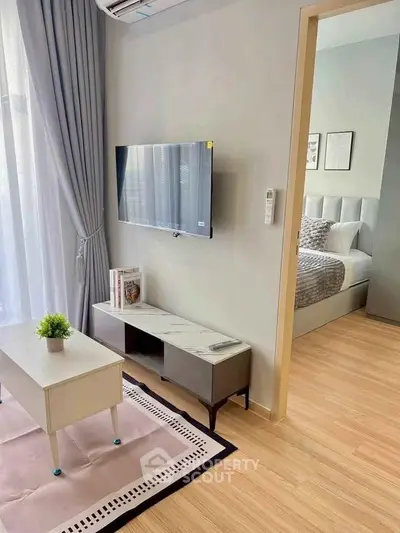 Modern living room with TV and view into cozy bedroom, featuring stylish decor and natural light.