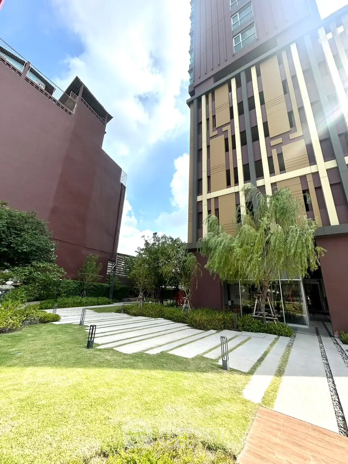 Modern building exterior with landscaped garden and pathway under a bright blue sky.