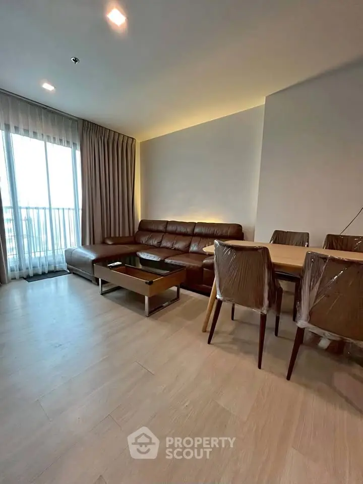 Modern living room with leather sofa and dining area, featuring large windows and elegant decor.