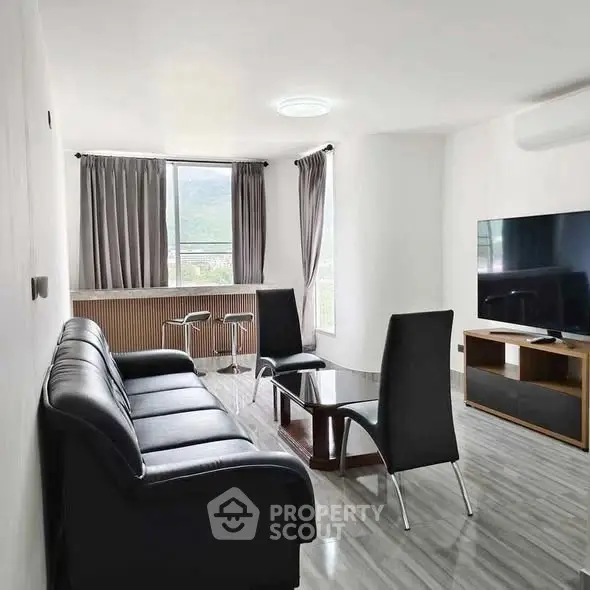 Modern living room with sleek black furniture and large TV, featuring a bright window view.