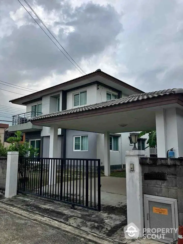 Charming two-story house with gated driveway and modern design under cloudy skies.