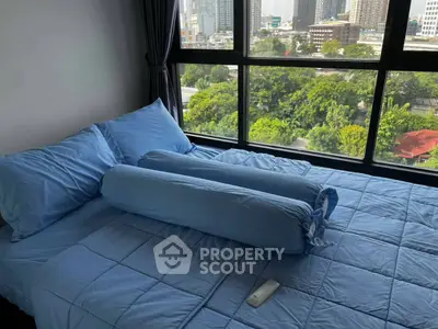 Cozy bedroom with large window offering stunning cityscape views, featuring a plush blue bedspread and pillows.