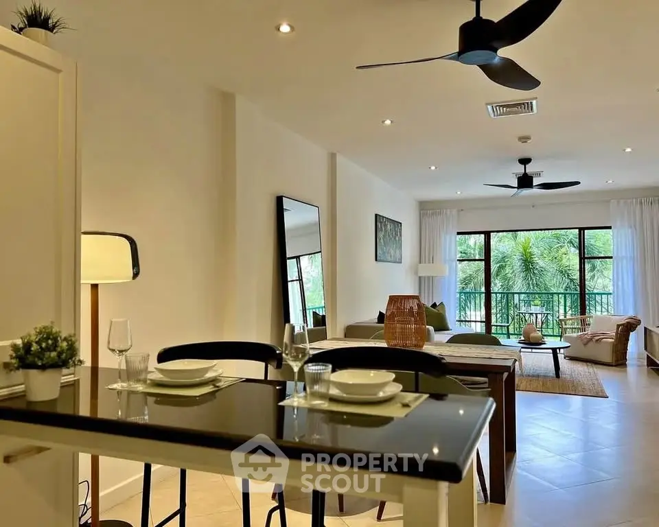 Spacious open-plan living room with modern decor and large windows overlooking greenery.