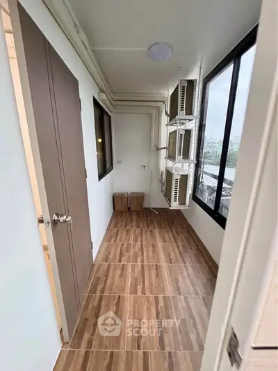 Compact storage room with wooden flooring and large windows in modern apartment.