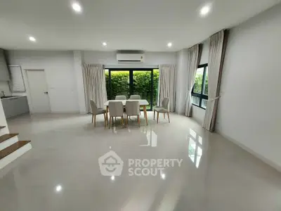 Spacious modern living room with dining area and large windows overlooking lush greenery.