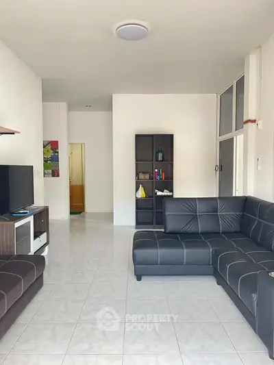 Spacious living room with modern black leather sofas and a flat-screen TV