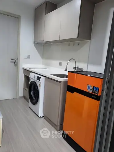 Modern kitchen with washing machine and vibrant orange fridge