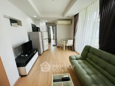 Modern living room with green sofa, TV, and dining area in open layout apartment.