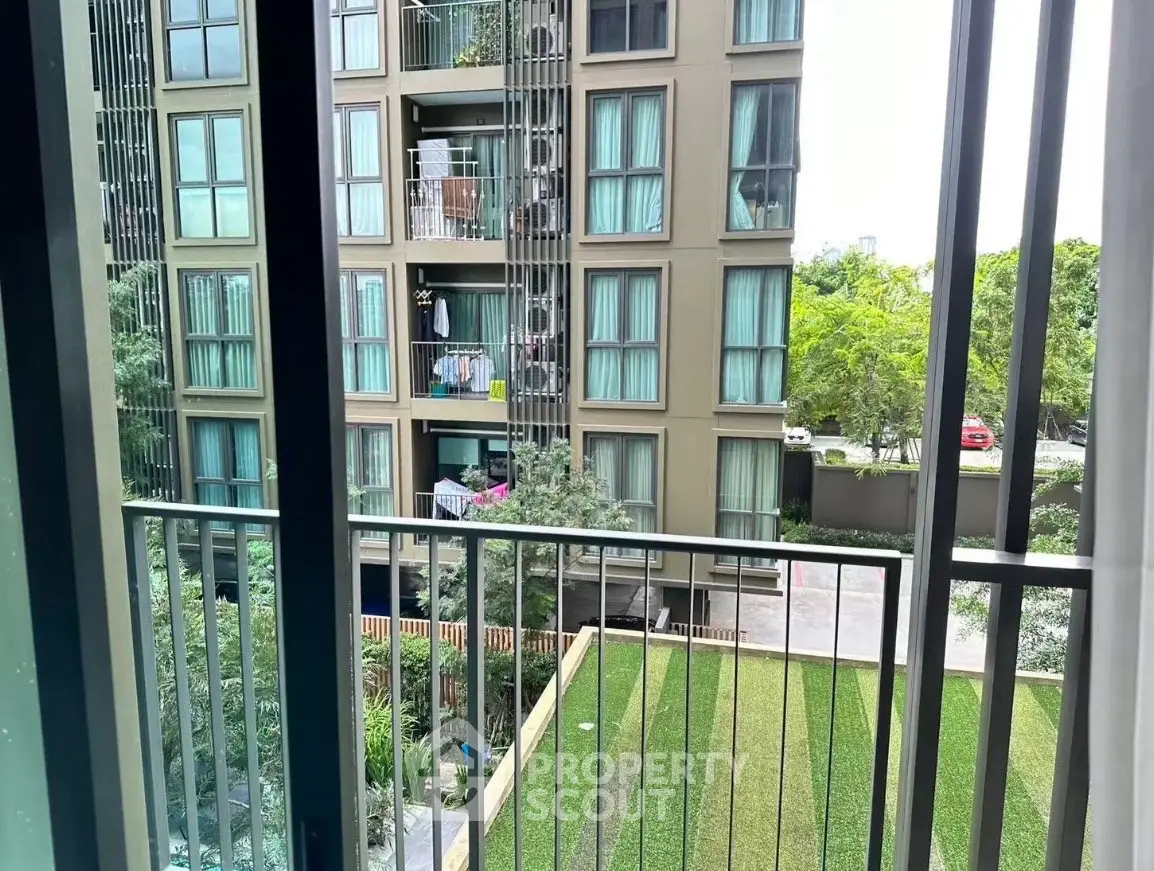 Modern apartment building view from balcony with lush greenery and urban surroundings.