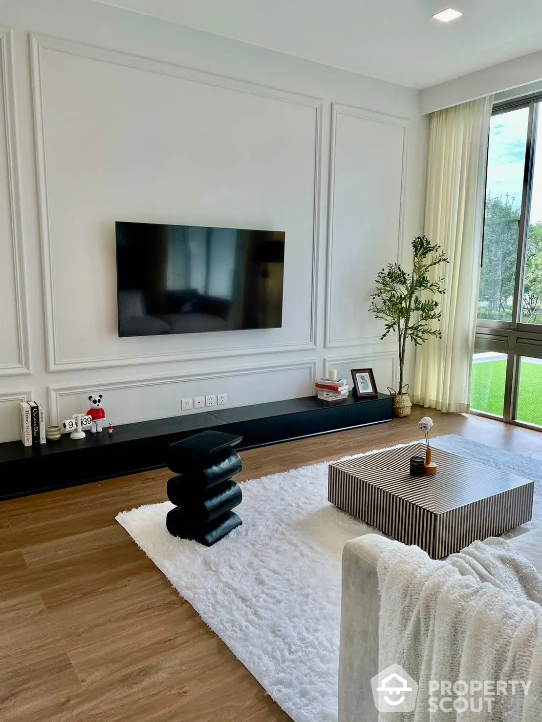 Elegant living room with classic wall paneling, hardwood floors, and a large window inviting natural light, complemented by modern furnishings.