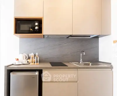 Modern kitchen with sleek cabinetry, microwave, and compact fridge in stylish apartment.