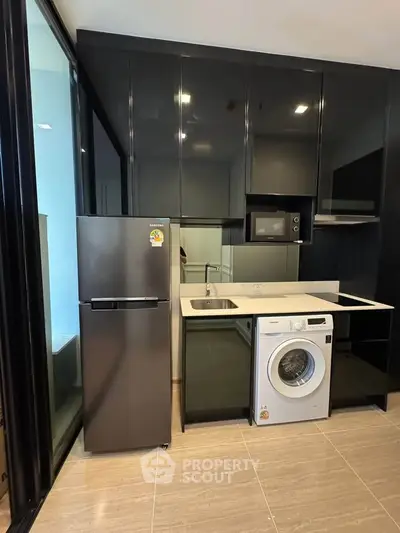 Modern kitchen with sleek black cabinets, fridge, and washing machine in a stylish apartment.