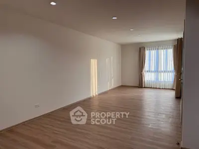 Spacious empty living room with wooden flooring and large window.
