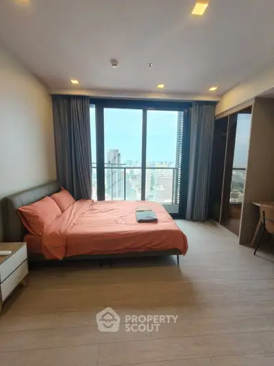 Spacious bedroom with city view and modern furnishings in high-rise apartment.