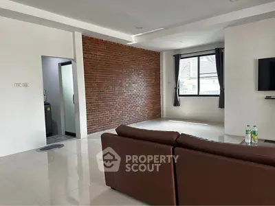 Spacious living room with modern brick accent wall and large window for natural light.