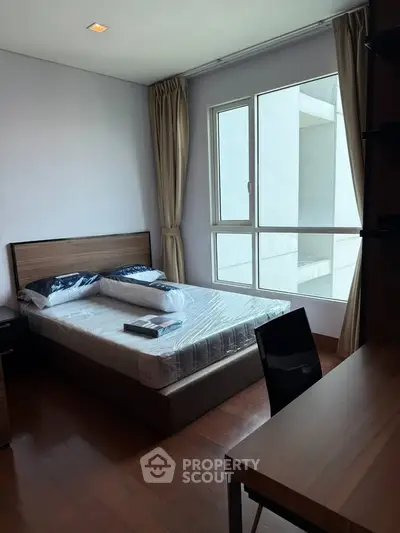 Modern bedroom with large window and wooden flooring in a stylish apartment.