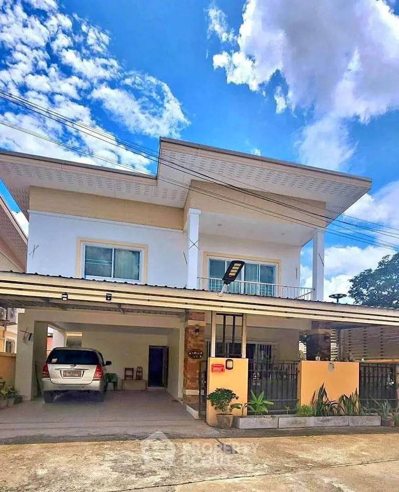 Modern two-story house with carport and balcony under a vibrant blue sky.