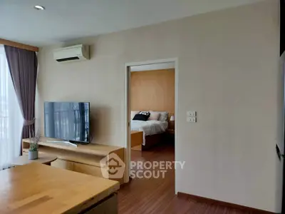 Modern apartment interior with open living room and bedroom view, featuring sleek furniture and natural light.