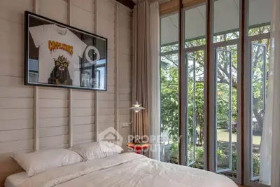 Cozy bedroom with large windows offering serene garden views and stylish decor.