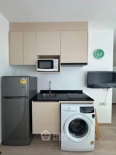 Modern kitchen with appliances including fridge, microwave, and washing machine in compact layout.