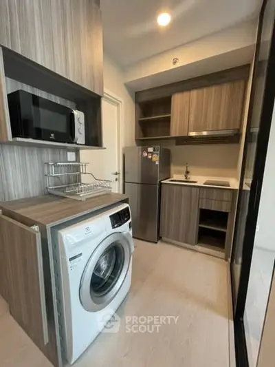 Modern kitchen with sleek wooden cabinets and built-in appliances, featuring a washing machine and compact fridge.