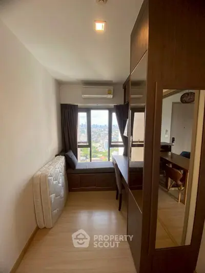 Compact bedroom with city view, featuring a large window, air conditioning, and wooden flooring.