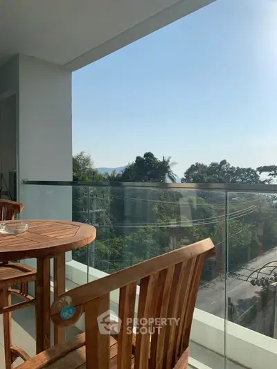 Spacious balcony with wooden furniture and scenic view of lush greenery.