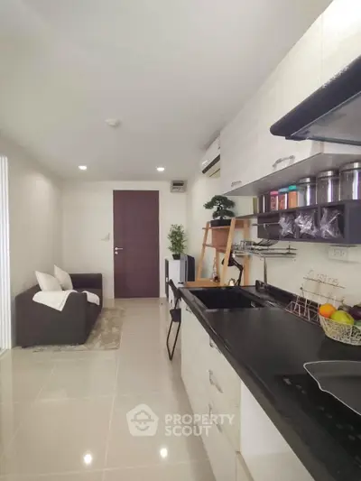 Modern kitchen with sleek black countertops and cozy living area in open layout apartment.