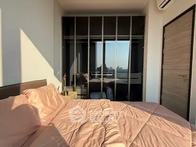 Modern bedroom with large mirrored wardrobe and city view, featuring soft pink bedding and sleek design.