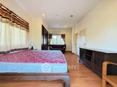 Spacious bedroom with wooden flooring and large windows for natural light.