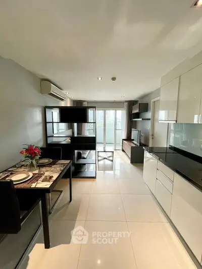 Modern open-plan living room with sleek kitchen and dining area, featuring large windows and stylish decor.